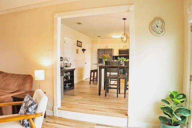 dining room with light wood-style floors, visible vents, crown molding, and baseboards