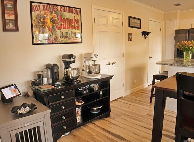 interior space featuring light wood-style flooring, visible vents, baseboards, ornamental molding, and freestanding refrigerator