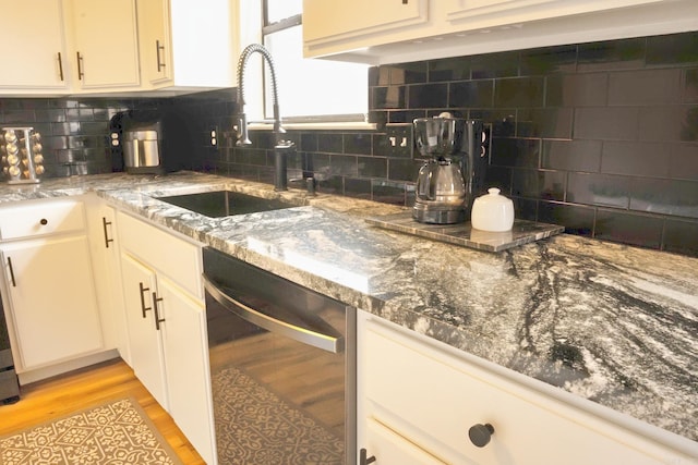 kitchen featuring a sink, light wood finished floors, backsplash, and stainless steel dishwasher