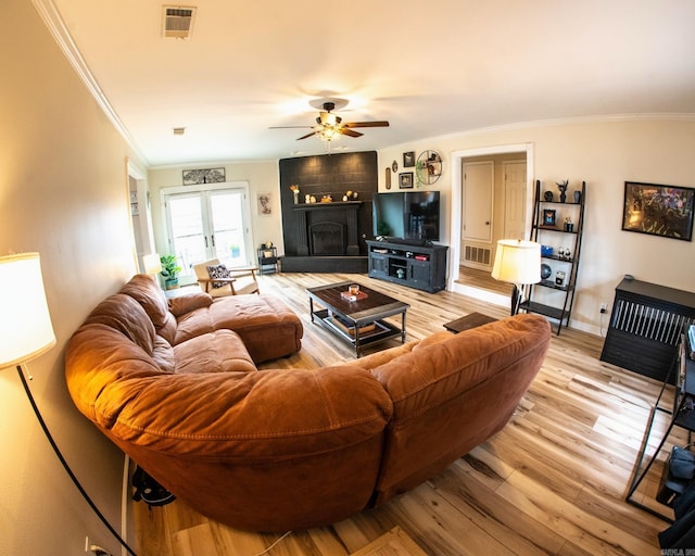 living room featuring light wood-style floors, a large fireplace, visible vents, and ornamental molding