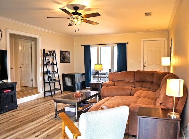 living room featuring light wood-type flooring, a ceiling fan, visible vents, and crown molding