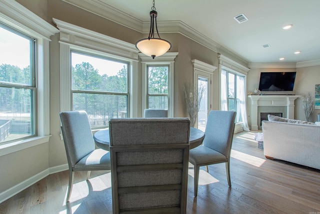 dining room featuring a fireplace, visible vents, ornamental molding, wood finished floors, and plenty of natural light