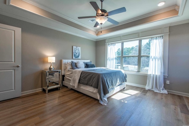 bedroom featuring baseboards, visible vents, wood finished floors, a tray ceiling, and crown molding