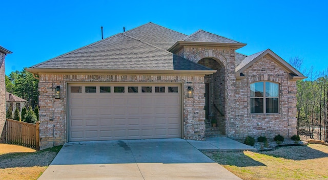 french country inspired facade with a shingled roof, concrete driveway, and an attached garage