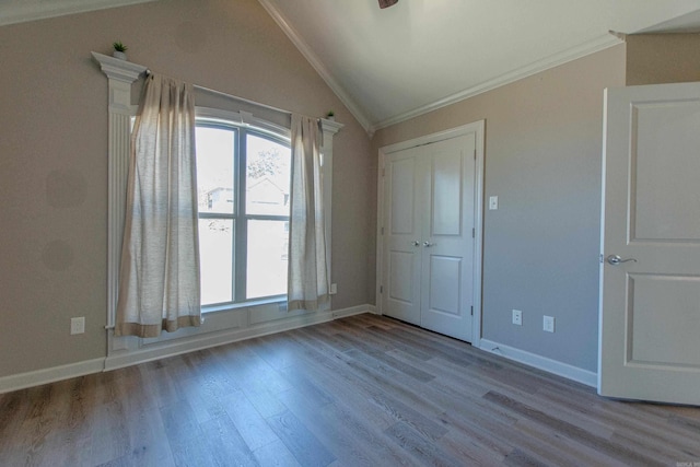 unfurnished bedroom with lofted ceiling, crown molding, baseboards, and wood finished floors
