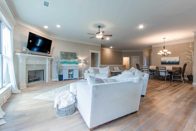 living area with visible vents, ceiling fan with notable chandelier, a fireplace, and light wood-style flooring