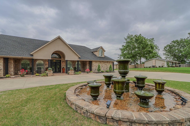 view of front of home featuring a shingled roof, stone siding, a front lawn, and stucco siding