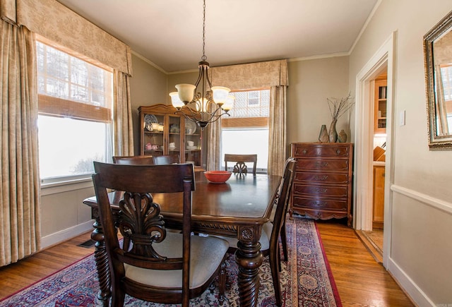 dining area featuring a notable chandelier, crown molding, baseboards, and wood finished floors