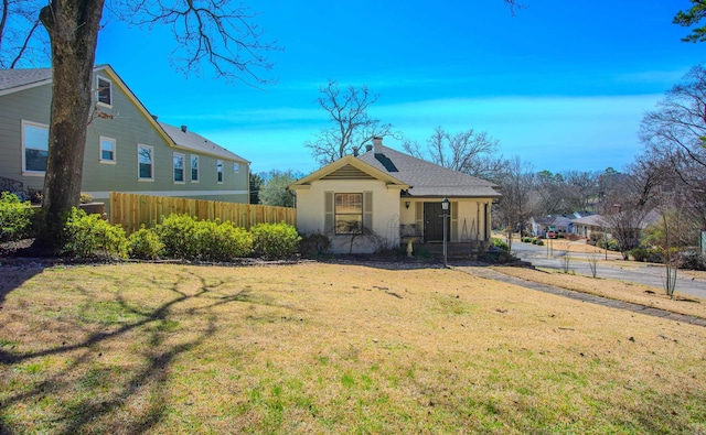 view of front of house with a shingled roof, a chimney, a front yard, and fence