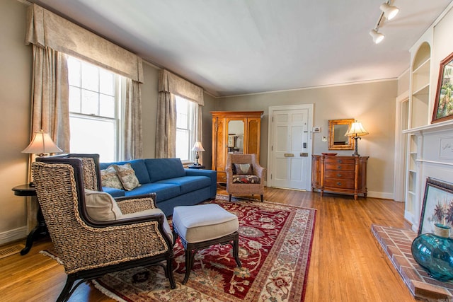 living area with light wood finished floors, a fireplace with raised hearth, visible vents, track lighting, and baseboards