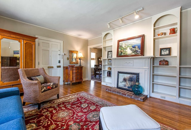 living area with baseboards, ornamental molding, wood finished floors, built in shelves, and a fireplace