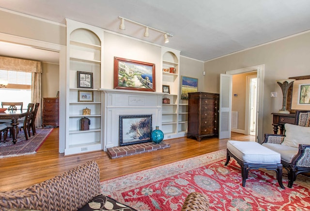 living area with ornamental molding, wood finished floors, a glass covered fireplace, and built in shelves