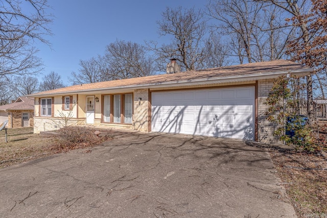 view of front of home featuring driveway, brick siding, a chimney, and an attached garage