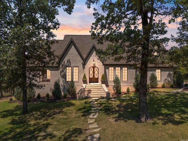 view of front facade with a front lawn, a shingled roof, and brick siding