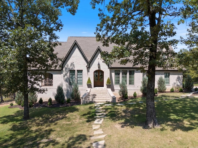 view of front of house with brick siding, a shingled roof, a front yard, and french doors