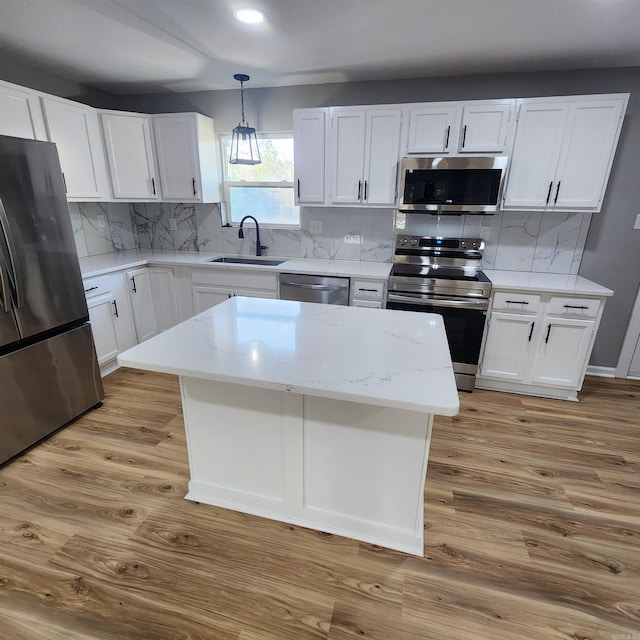 kitchen featuring white cabinets, light wood-style flooring, appliances with stainless steel finishes, a sink, and backsplash