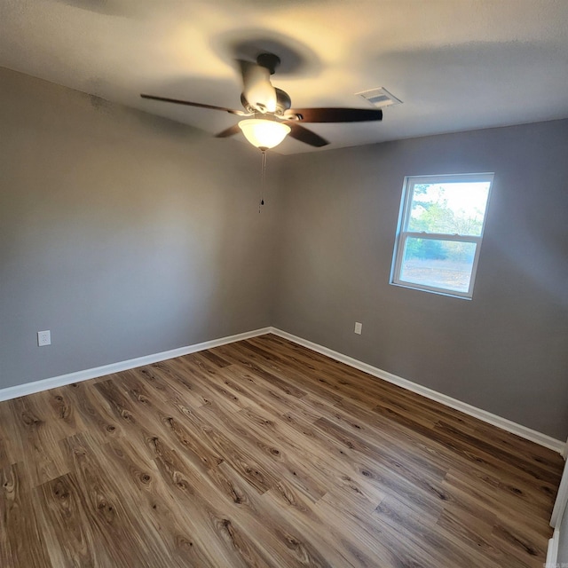 spare room featuring a ceiling fan, visible vents, baseboards, and wood finished floors