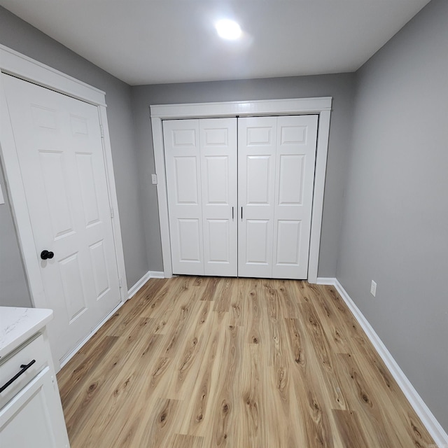 unfurnished bedroom featuring a closet, baseboards, and light wood finished floors