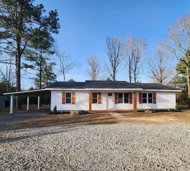 single story home featuring gravel driveway, covered porch, and a carport