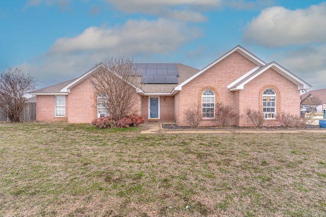 single story home with a shingled roof, brick siding, a front lawn, and solar panels