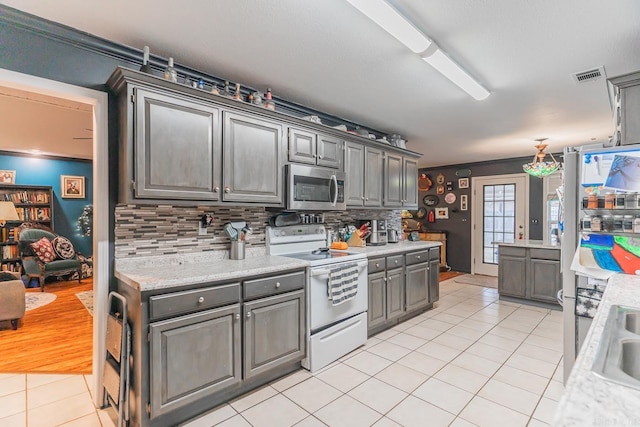 kitchen with light tile patterned floors, stainless steel appliances, gray cabinets, and decorative backsplash