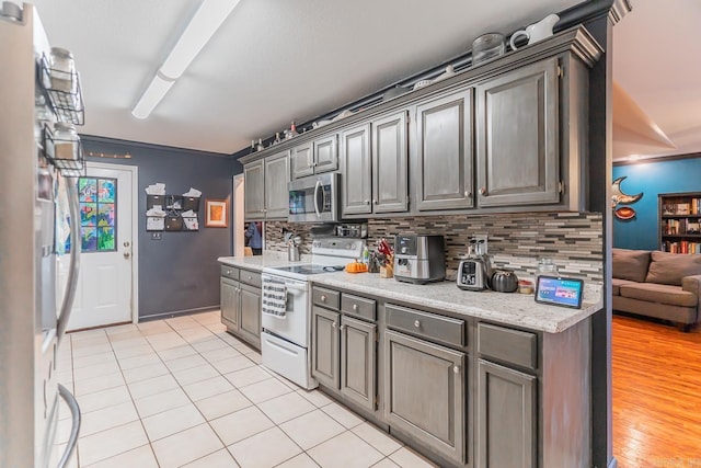 kitchen featuring appliances with stainless steel finishes, gray cabinets, light tile patterned flooring, and decorative backsplash