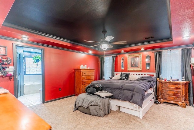 carpeted bedroom with ornamental molding, a tray ceiling, connected bathroom, and a ceiling fan