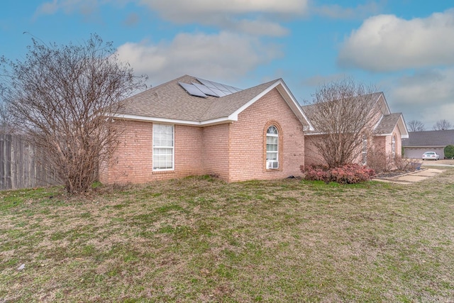 view of side of home featuring a yard, a shingled roof, roof mounted solar panels, and brick siding