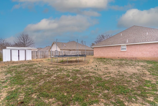 view of yard with a trampoline, an outbuilding, a fenced backyard, and a shed