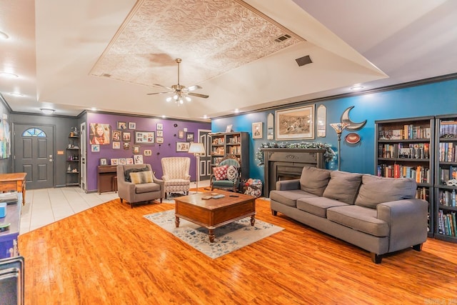 living area with a fireplace, wood finished floors, a ceiling fan, and crown molding