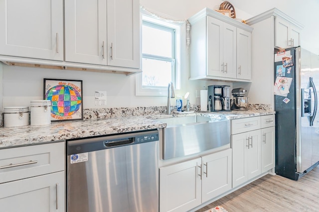 kitchen featuring light stone counters, light wood-style flooring, a sink, white cabinets, and appliances with stainless steel finishes