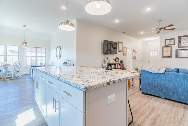 kitchen with light wood-style flooring, a kitchen island, ornamental molding, open floor plan, and light stone countertops