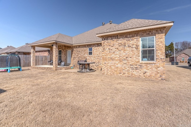 rear view of house with a patio, brick siding, fence, roof with shingles, and a trampoline