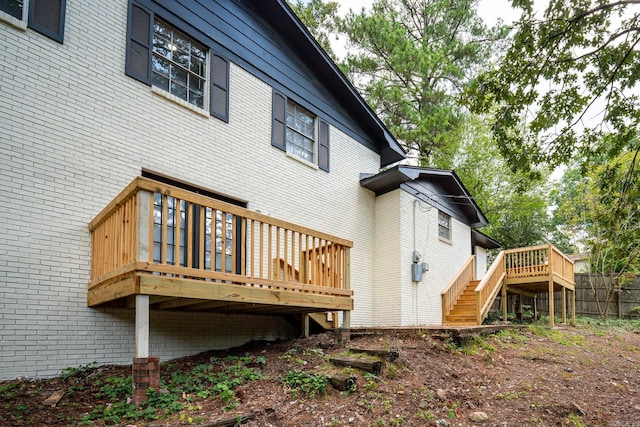 view of side of home with brick siding, fence, stairway, and a wooden deck