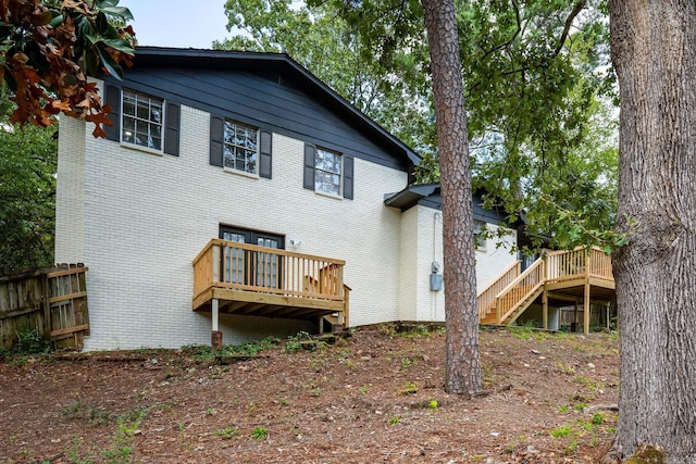 rear view of property with a wooden deck, stairs, fence, and brick siding