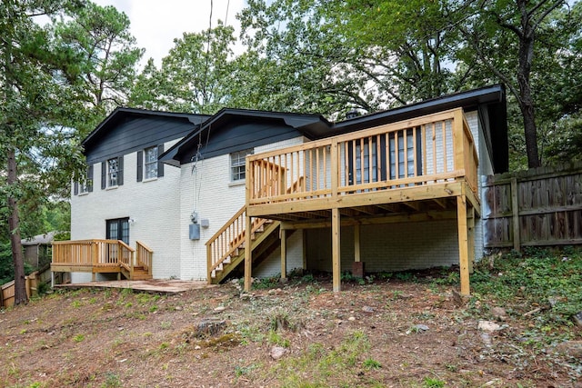 rear view of house featuring a wooden deck, fence, and brick siding