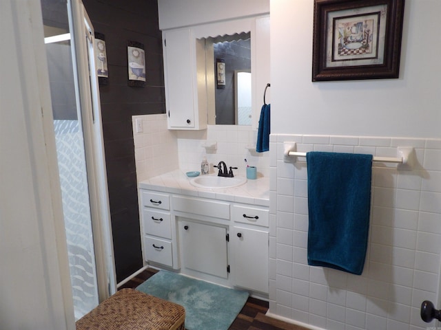 full bath with a stall shower, a wainscoted wall, vanity, and tile walls