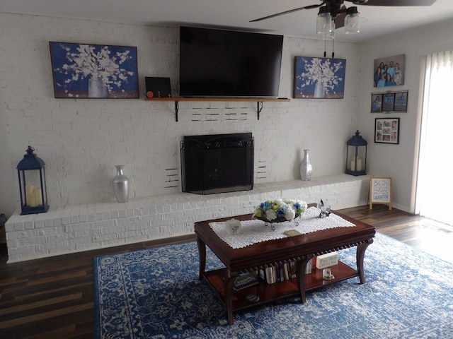 living room with brick wall, ceiling fan, a fireplace, and wood finished floors