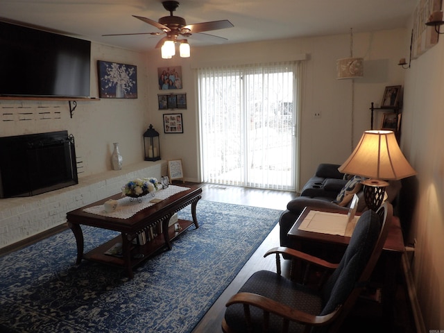 living area featuring a ceiling fan, a brick fireplace, and wood finished floors