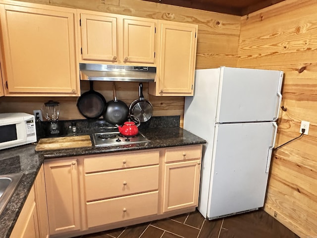 kitchen with wood walls, dark stone countertops, under cabinet range hood, and white appliances