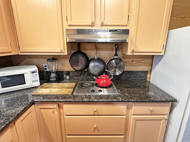 kitchen featuring decorative backsplash, under cabinet range hood, dark stone counters, and white appliances