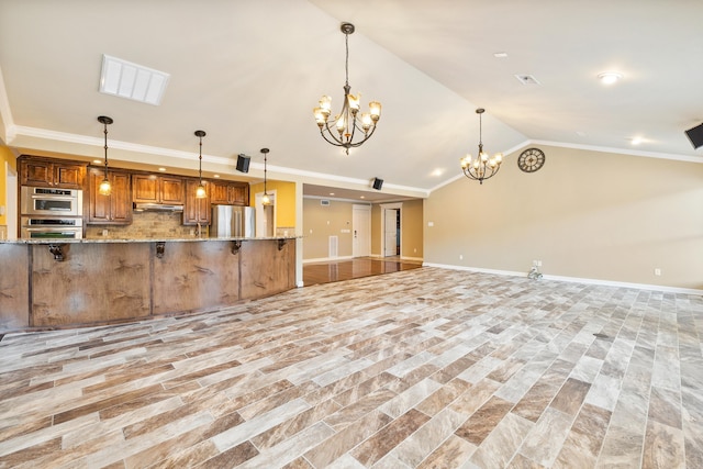 kitchen with tasteful backsplash, appliances with stainless steel finishes, brown cabinetry, ornamental molding, and vaulted ceiling