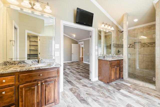 full bathroom with lofted ceiling, two vanities, a sink, a stall shower, and crown molding