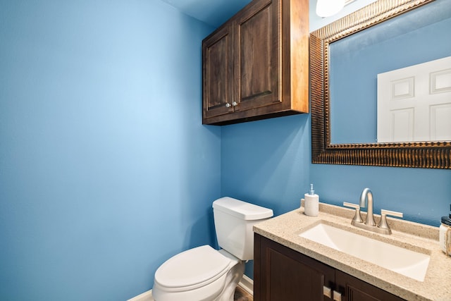 half bathroom featuring toilet, baseboards, and vanity