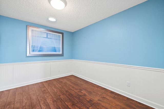 spare room with a textured ceiling, dark wood-type flooring, and wainscoting