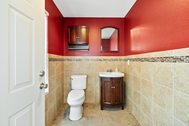 half bathroom with toilet, a wainscoted wall, tile patterned floors, vanity, and tile walls