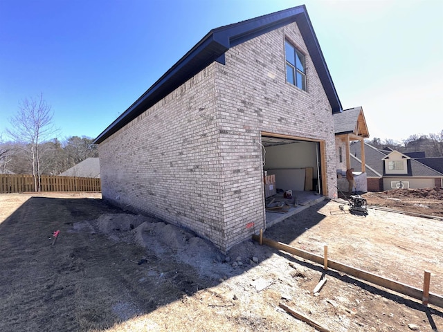 view of side of home with brick siding, fence, and an attached garage