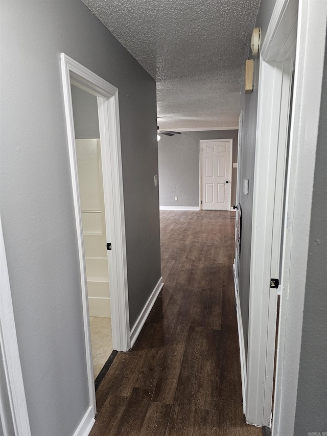 hall with a textured ceiling, dark wood-type flooring, and baseboards