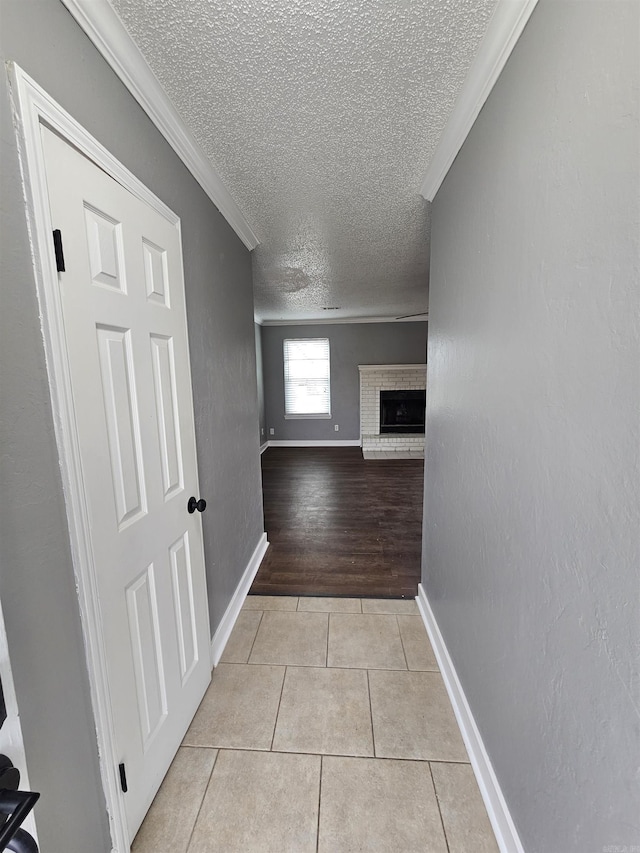 hall with light tile patterned floors, a textured ceiling, baseboards, and crown molding