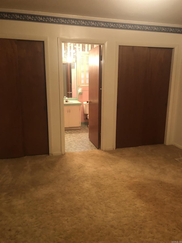 unfurnished bedroom with ensuite bath, a closet, a sink, and light colored carpet